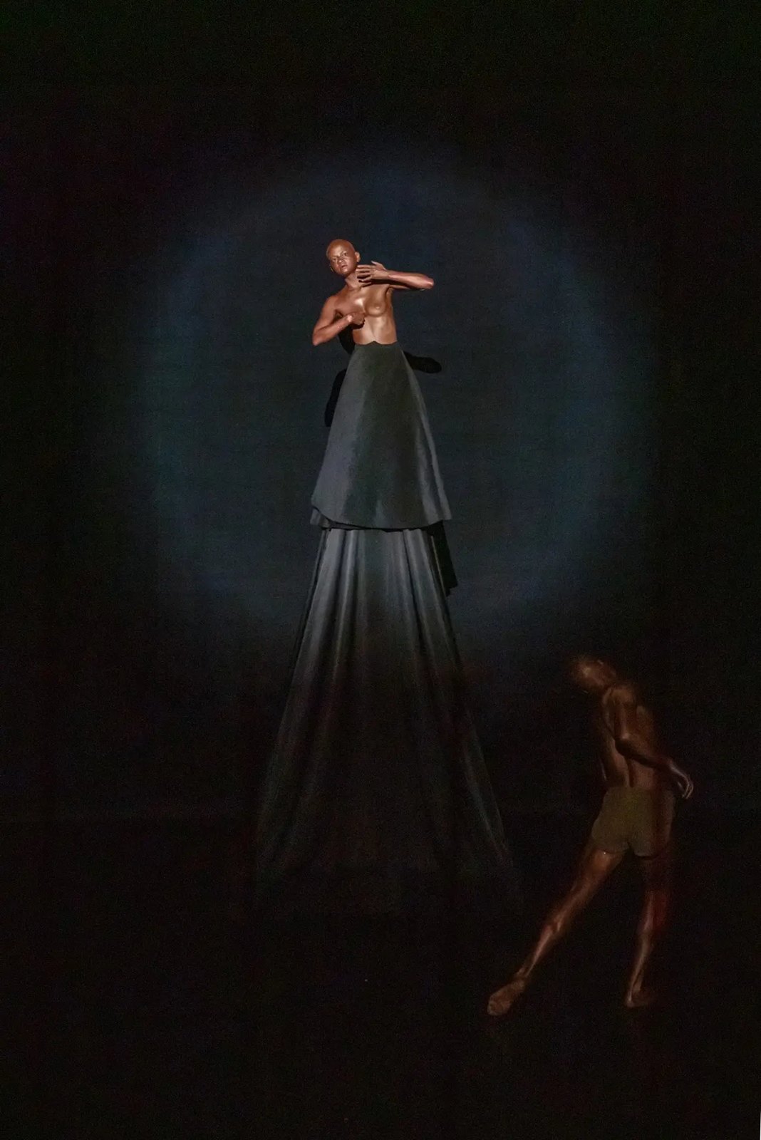 Performer raised on a tall dark cone of fabric inside a halo of light in BLACK VELVET