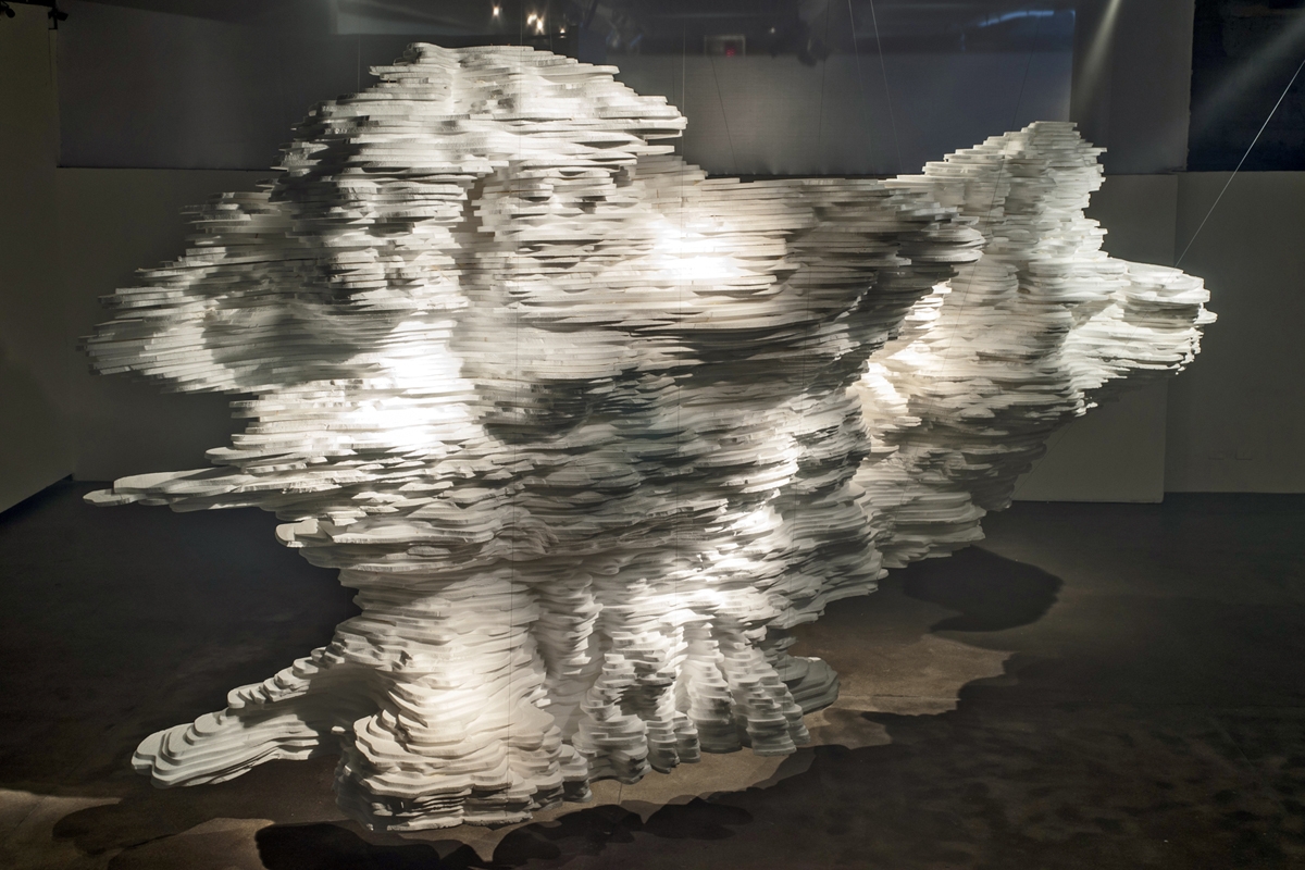 Sculpted white paper mass filling the corner of a dim exhibition room