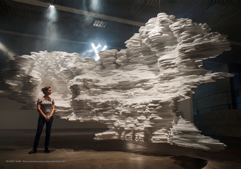 A visitor standing beneath the suspended white paper cloud sculpture of In Void at MuBE, São Paulo